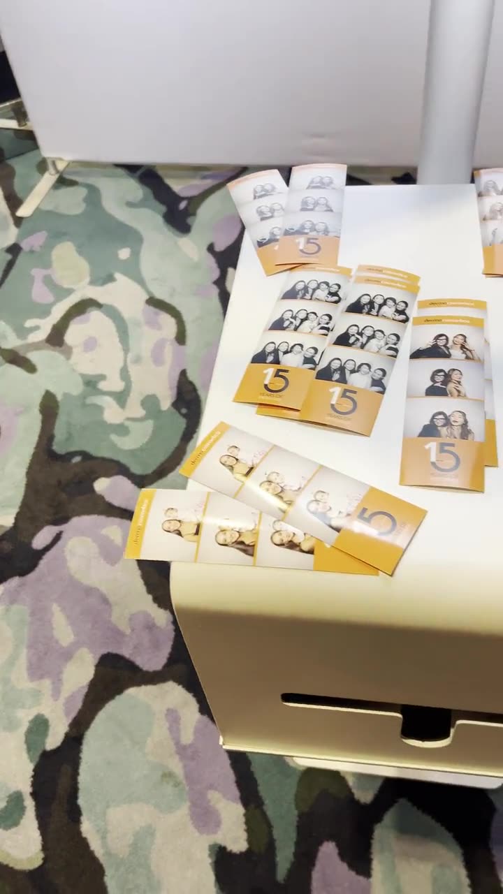 Orange and white branded photo booth strips marked 15 Years of Excellence laid out on top of a white booth printer
