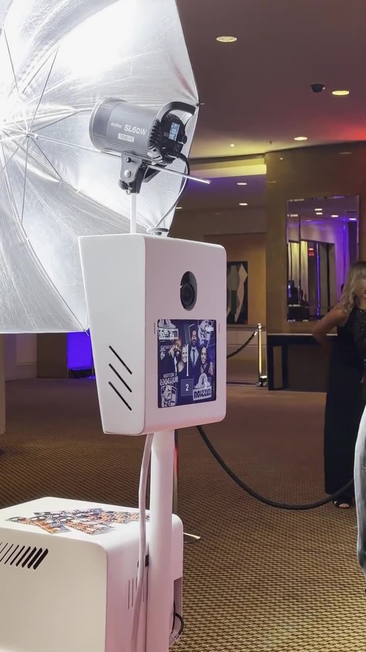 White photo booth with a silver umbrella light and a screen showing a strip preview with Western Bulldogs and Mission logos, in a carpeted function room with a rope barrier