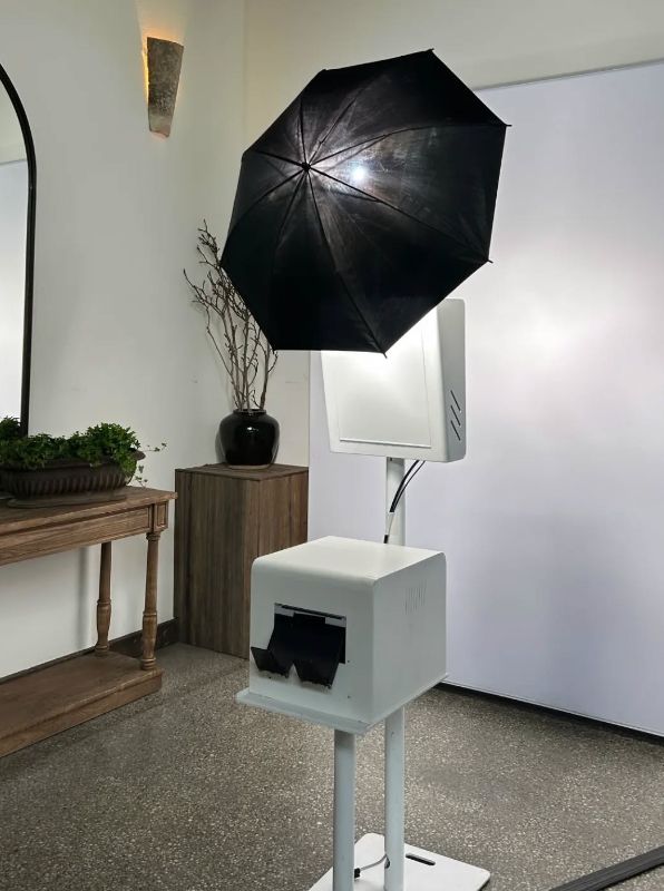 Ghost Booth Events photo booth set up with an umbrella light above the camera unit and a white printer on a stand in front of a light grey backdrop