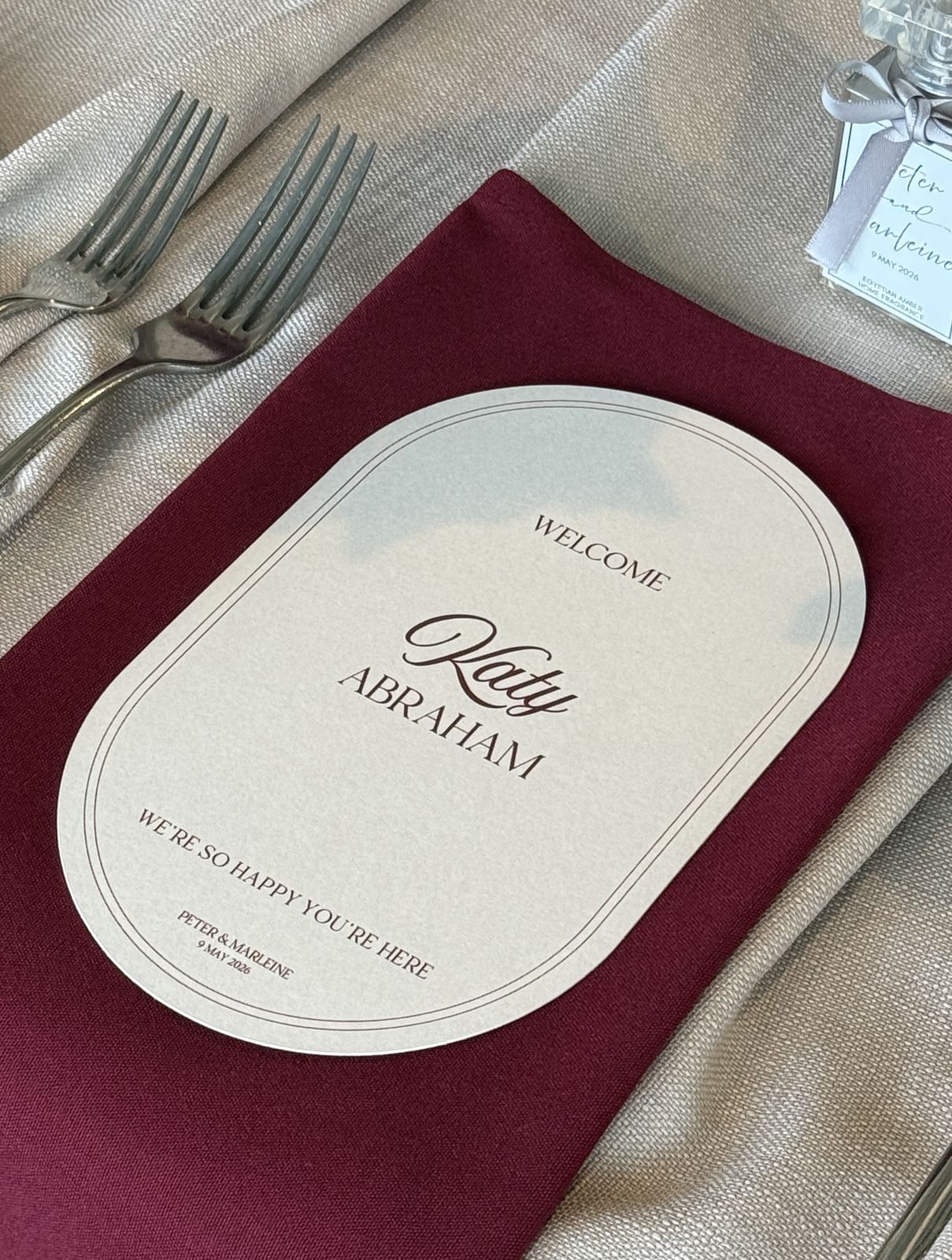 Oval welcome place card on a burgundy napkin at a wedding reception table setting