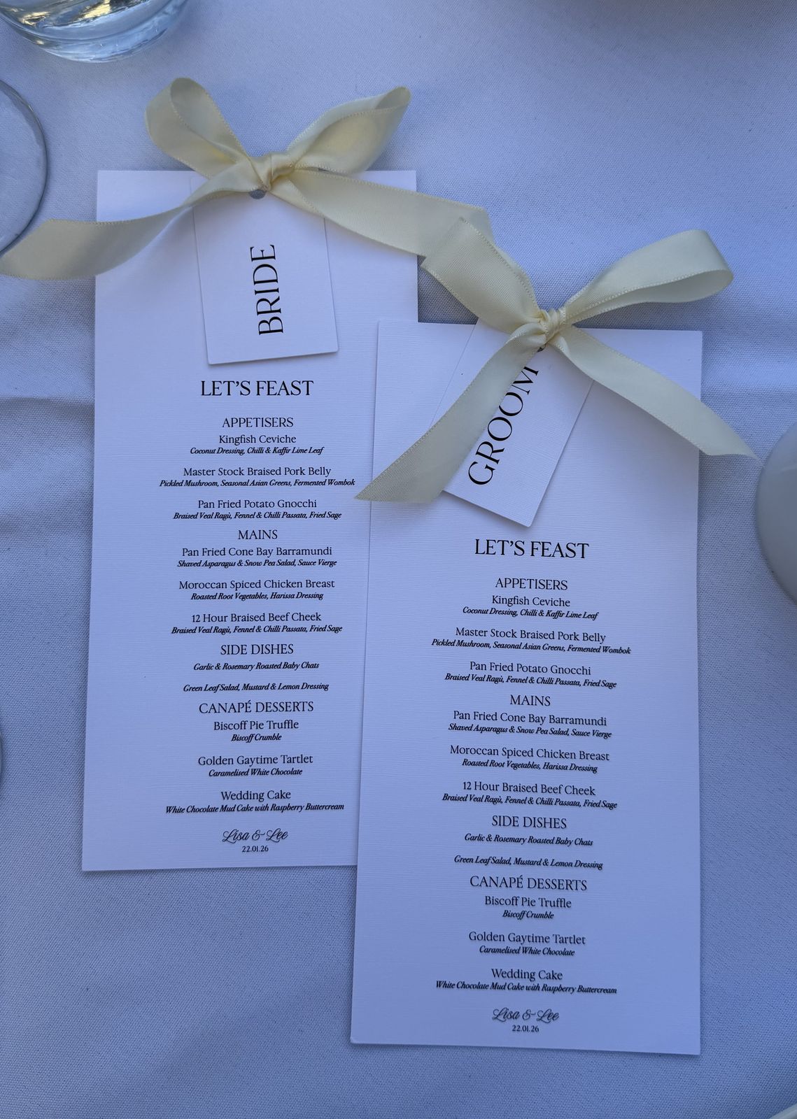 Two printed wedding menus tied with ivory ribbon, laid flat on a blue background
