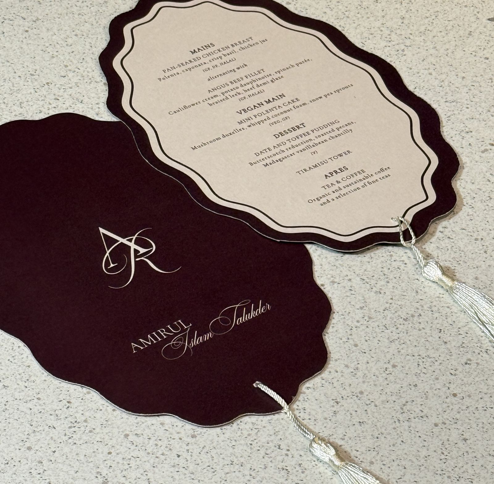 Scalloped burgundy and ivory wedding menu with a monogram, photographed on a reception table