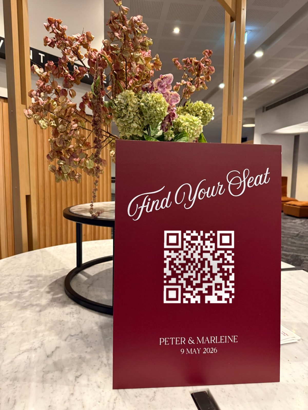 Burgundy Find Your Seat sign with a QR code on a marble table