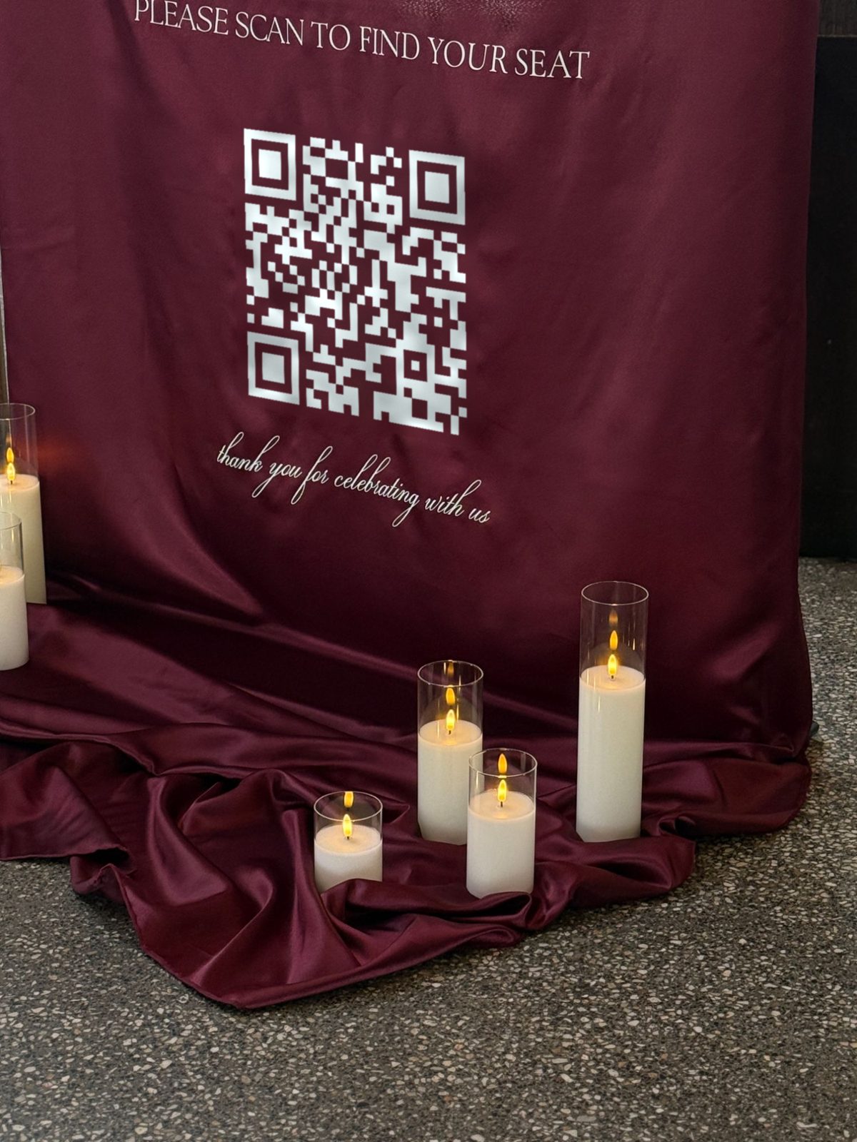 Burgundy satin sign with a white QR code, draped onto the floor and styled with candles
