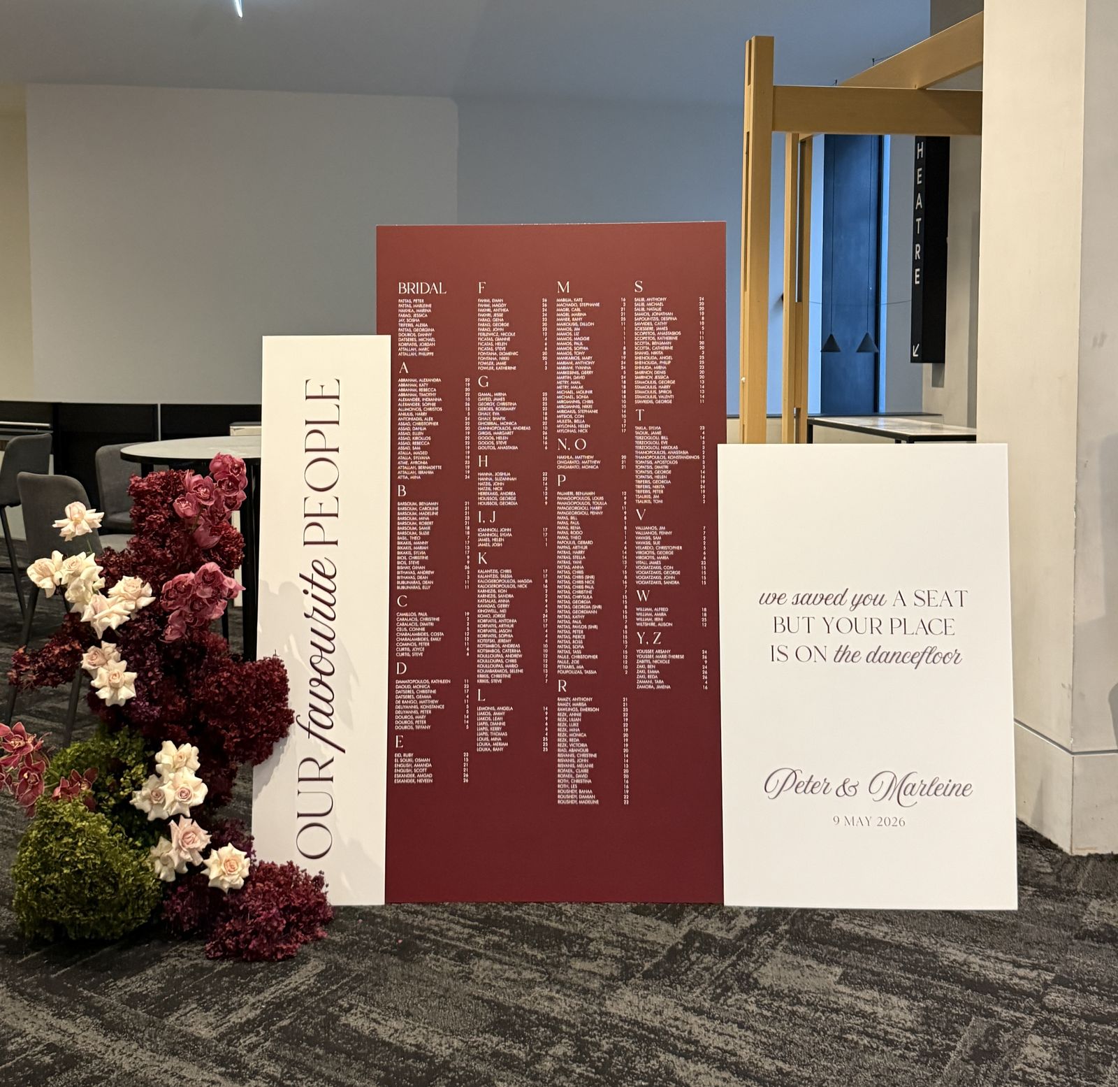 Burgundy alphabetical seating chart between a narrow white panel reading Our favourite people and a white sign reading we saved you a seat but your place is on the dancefloor