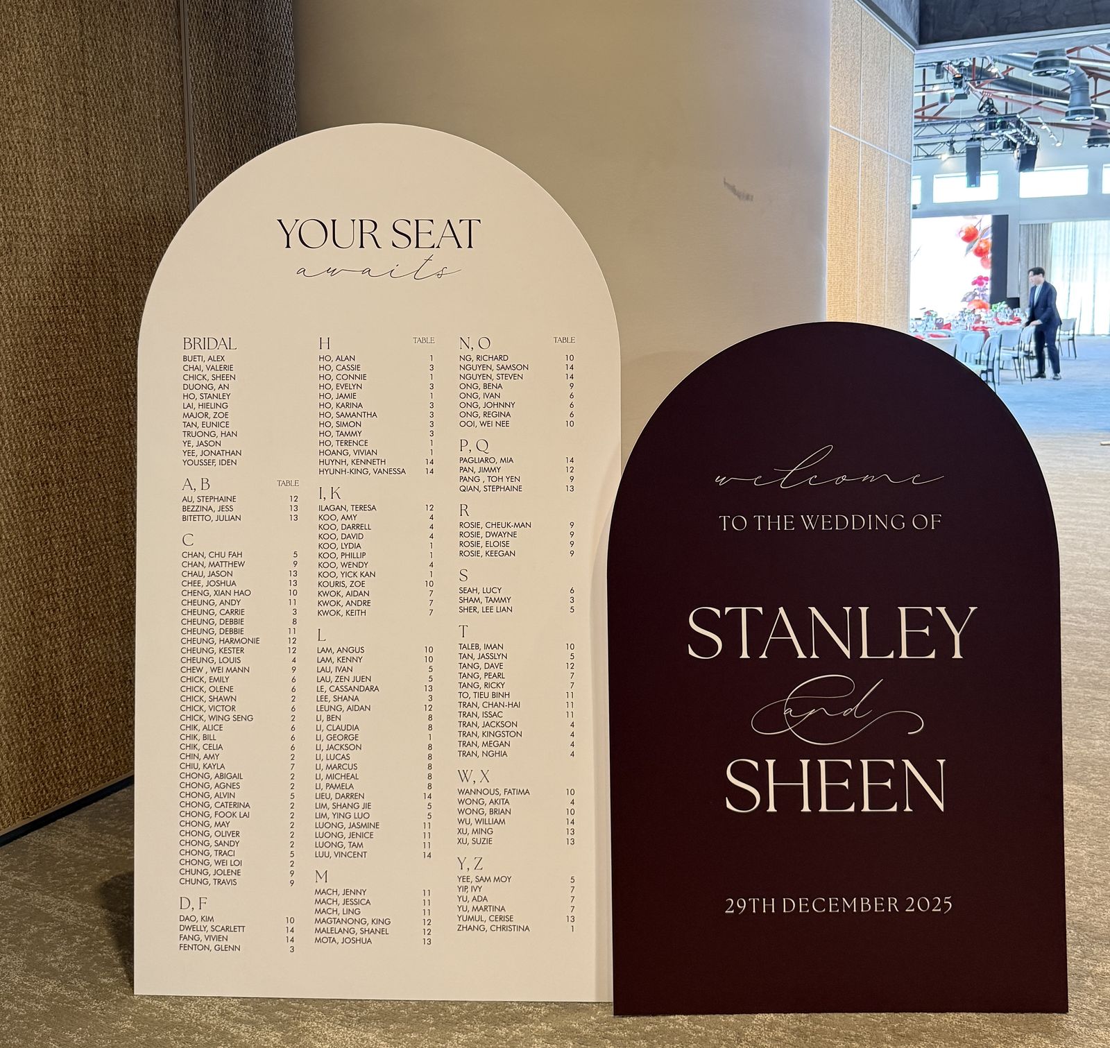 Plum arch welcome sign with cream lettering for Stanley and Sheen, standing in front of a cream arch seating chart