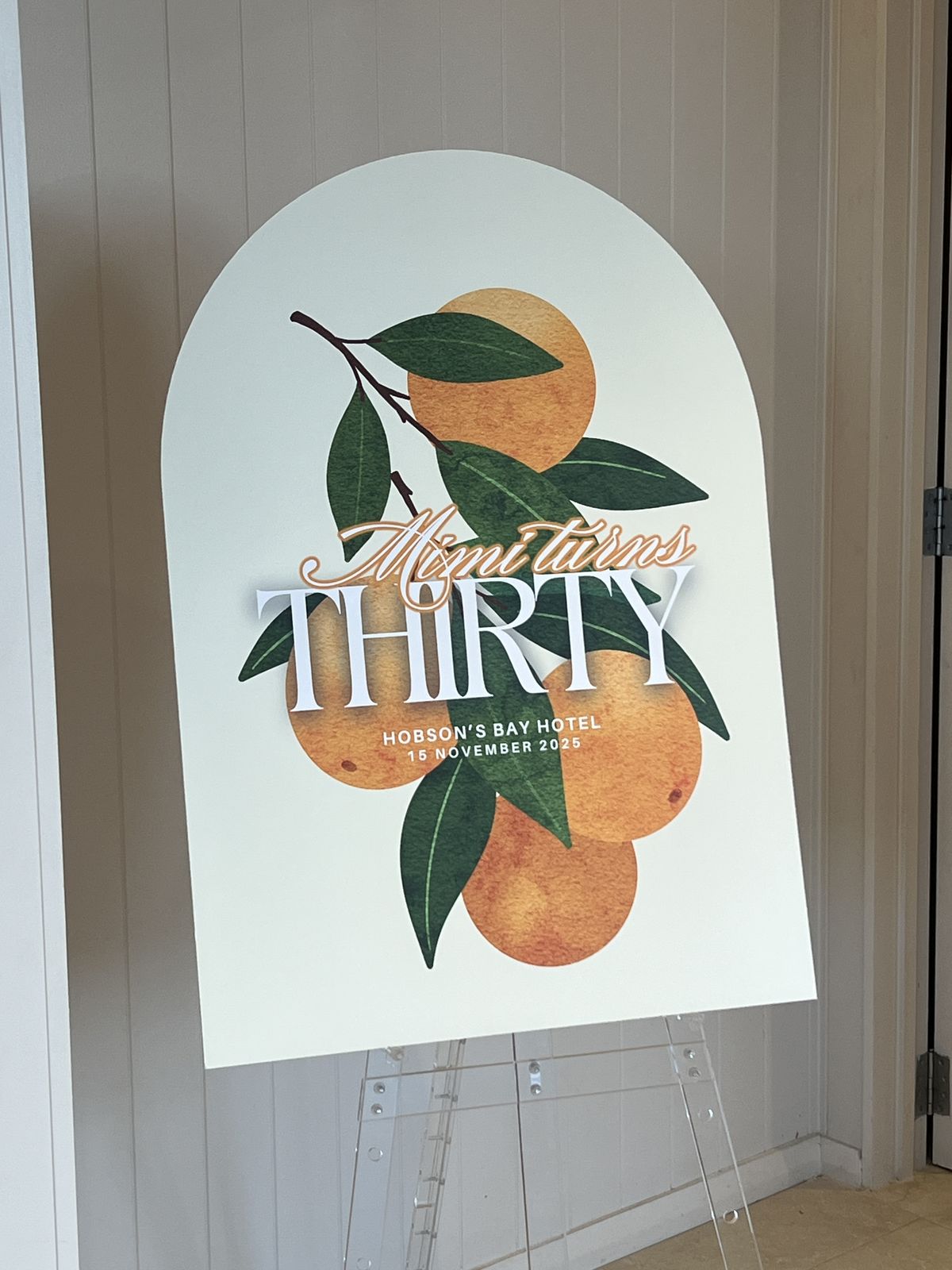 Arched birthday sign with an orange-tree illustration and gold lettering, displayed on an easel