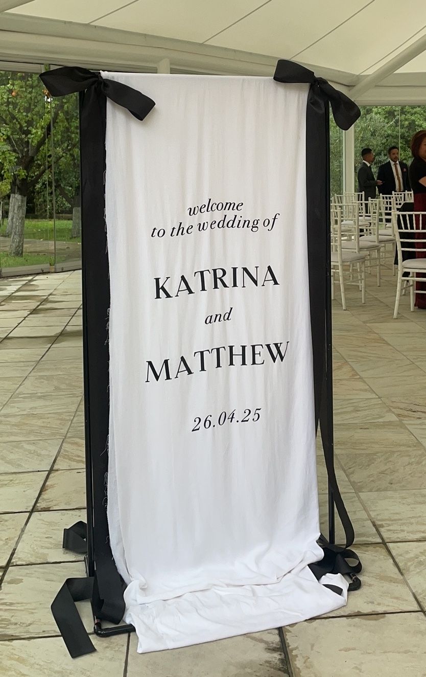 White linen welcome sign for Katrina and Matthew hung from a stand with large black bows and black ribbon tails