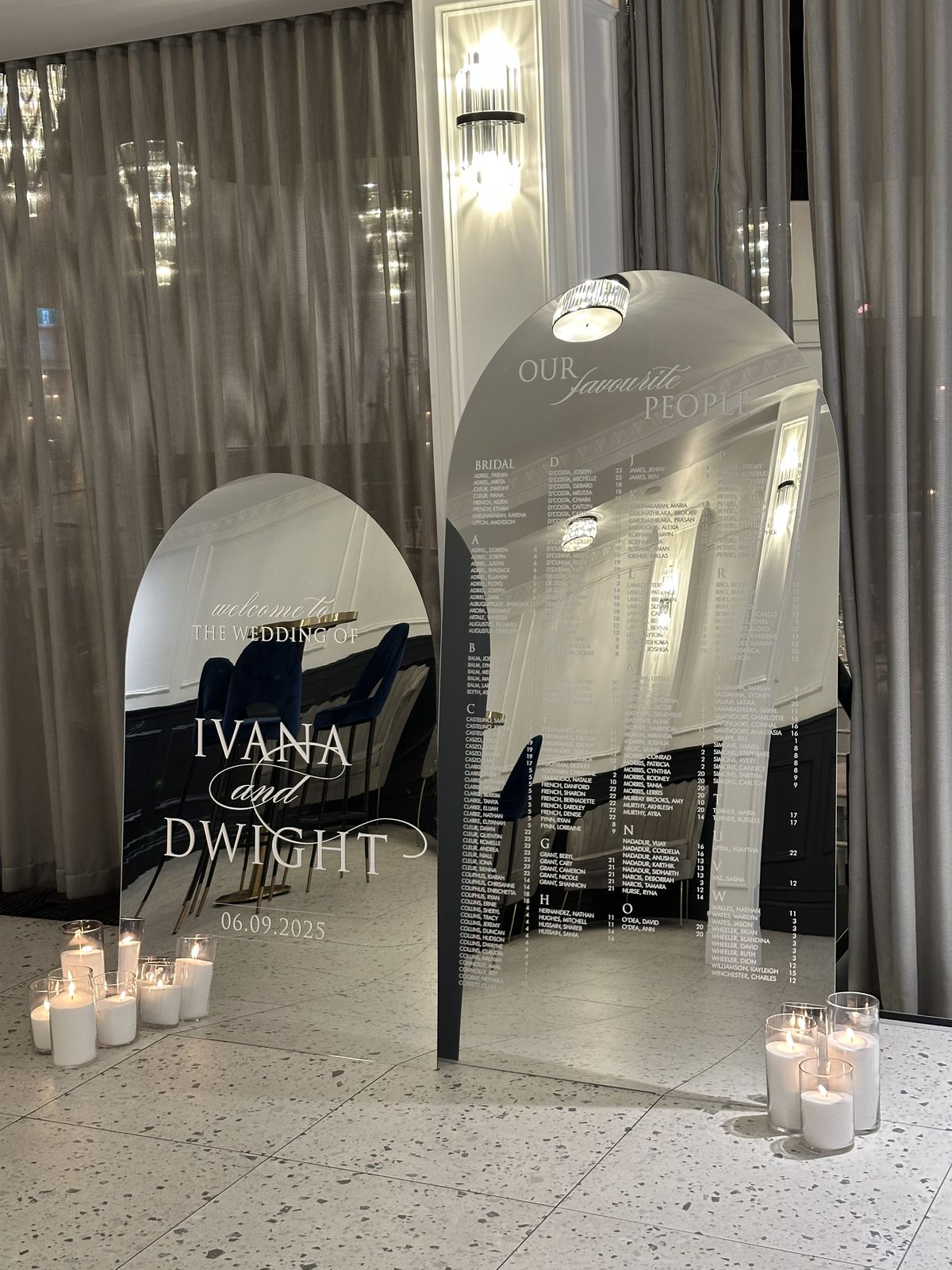 Two silver mirror arches on a terrazzo floor, a shorter welcome sign for Ivana and Dwight and a taller Our favourite people seating chart, with pillar candles at the base